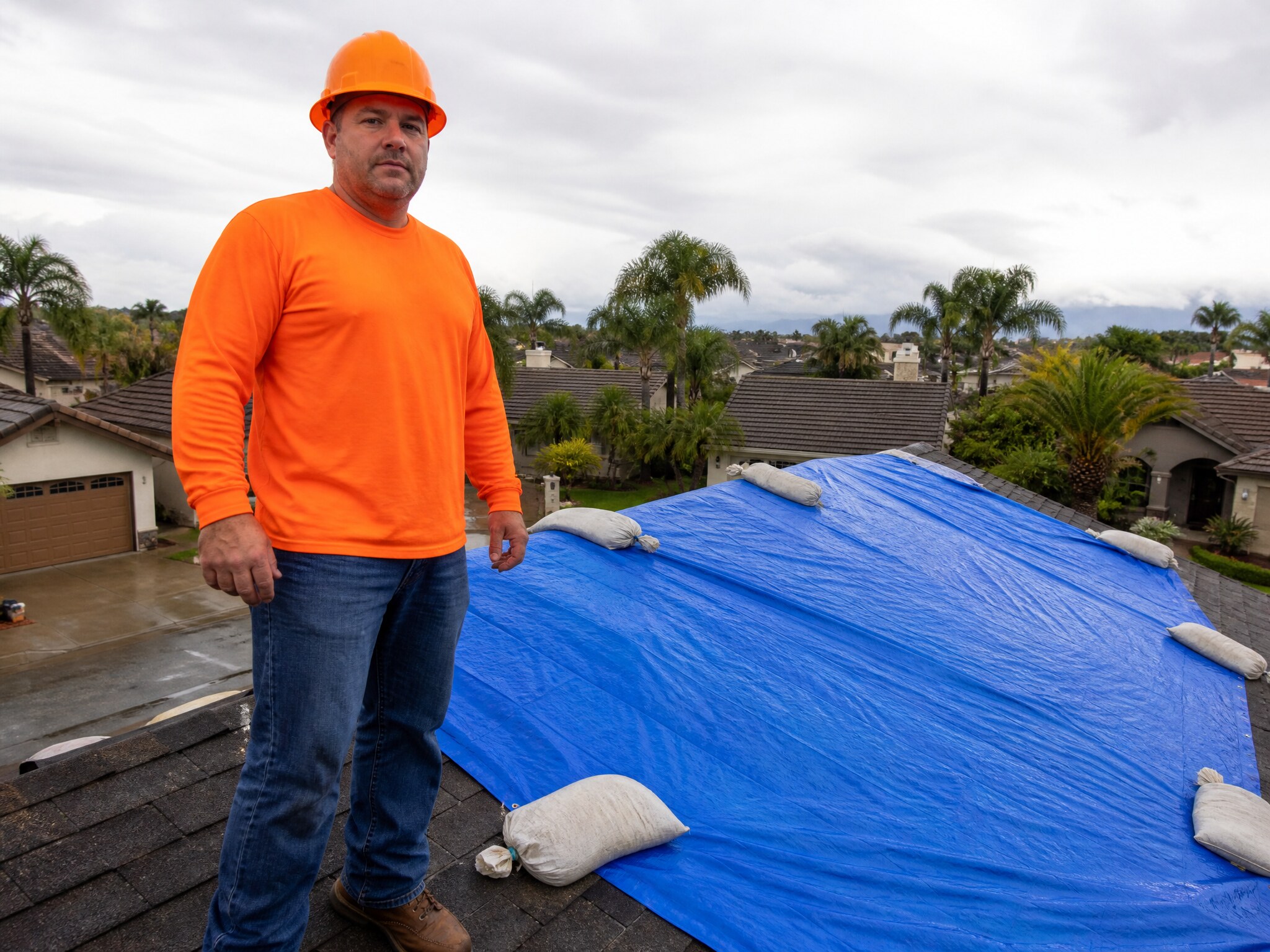 Blue emergency tarp secured over a storm-damaged residential roof